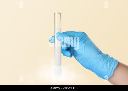 Crioconservazione. Assistente di laboratorio che tiene provetta con sperma su fondo beige, primo piano. Effetto gelo Foto Stock