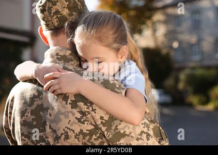 Figlia che abbraccia suo padre in uniforme militare Ucraina all'aperto. Ricongiungimento familiare Foto Stock