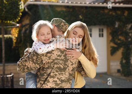 Figlia e moglie che abbraccia soldato in uniforme militare Ucraina all'aperto. Ricongiungimento familiare Foto Stock