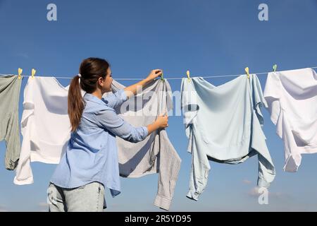 Donna appendere abiti con clothespins sulla linea di lavaggio per asciugare contro cielo blu Foto Stock