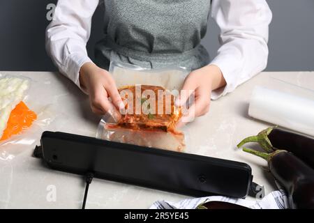 Donna che usa sigillante per confezionamento sottovuoto su tavolo in marmo bianco, primo piano Foto Stock