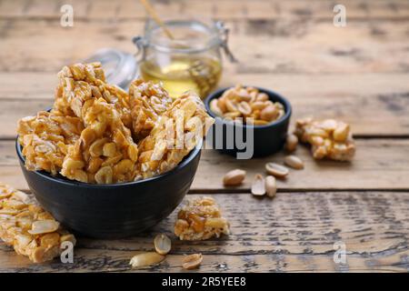 Deliziose barrette kozinaki di arachidi in ciotola su tavolo di legno, spazio per il testo Foto Stock