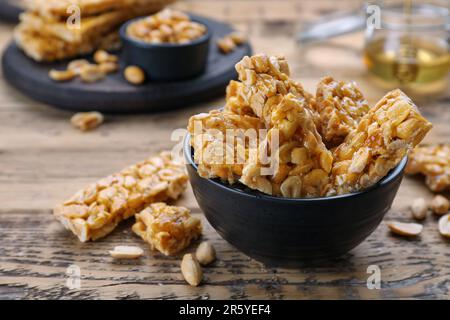 Deliziose barrette kozinaki di arachidi in ciotola su tavolo di legno, spazio per il testo Foto Stock