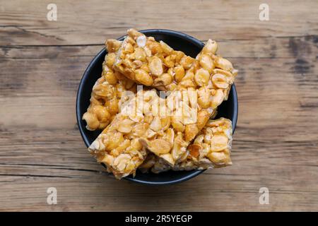 Deliziose barrette kozinaki di arachidi in ciotola su tavolo di legno, vista dall'alto Foto Stock