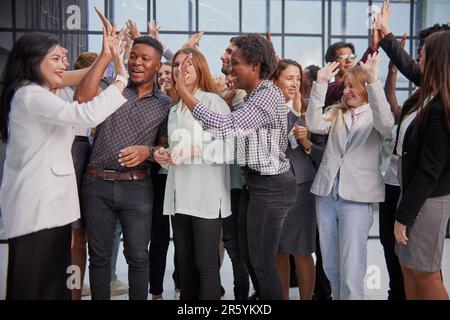 Dipendenti multinazionali entusiasti che celebrano la vittoria del team, offrendo cinque persone riunite in carica, Foto Stock