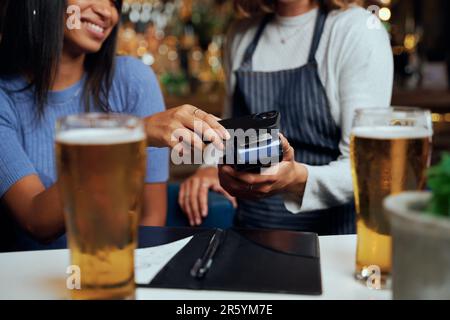 Giovane donna in abbigliamento casual che paga per cena con tecnologia wireless accanto alla cameriera Foto Stock