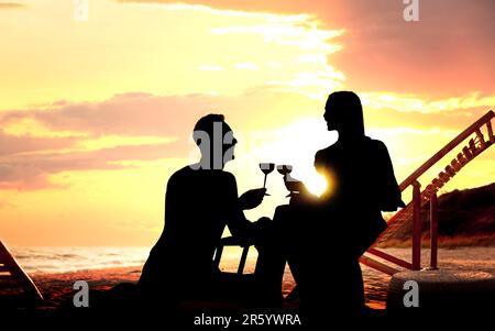 La silhouette di una bella coppia che beve vino insieme sulla spiaggia al tramonto Foto Stock