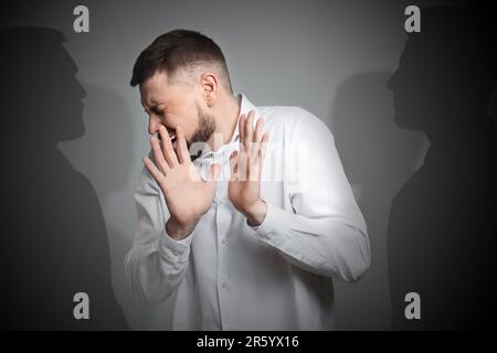 Che soffre di allucinazioni. Spaventato l'uomo che ha delusione come ombre di persone che lo circondano su sfondo grigio Foto Stock