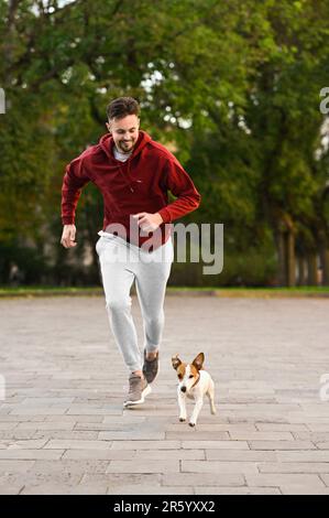 Uomo che corre con l'adorabile Jack Russell Terrier sulla strada cittadina. Cane a piedi Foto Stock