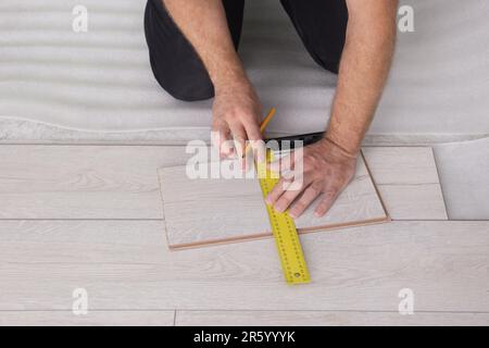 Uomo che usa il metro a nastro durante l'installazione di pavimenti in laminato, primo piano Foto Stock