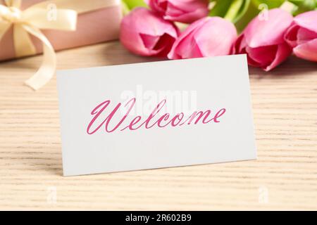 Welcome card, confezione regalo e bellissimi tulipani rosa su tavolo di legno, primo piano Foto Stock