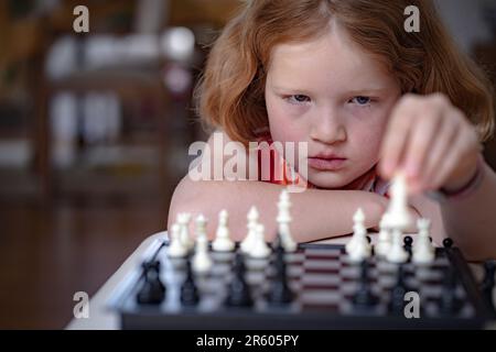 Una ragazza dai capelli rossi che gioca a scacchi, pensando di riflettere sulla mossa successiva. Messa a fuoco differenziale, primo piano. Foto Stock