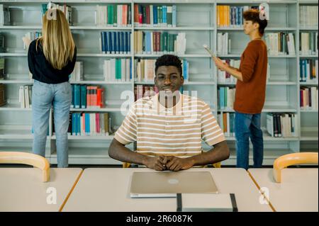 Felice giovane uomo nero seduto con un computer portatile chiuso Foto Stock