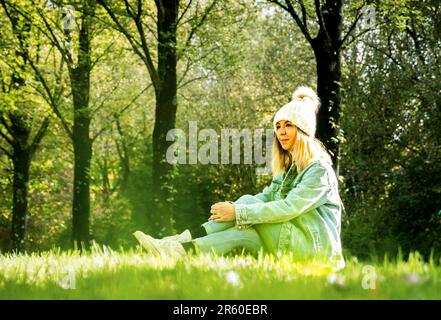 Un attraente modello femminile che indossa un elegante cappello si trova in un lussureggiante campo erboso verde, che colpisce una posa per la fotocamera Foto Stock