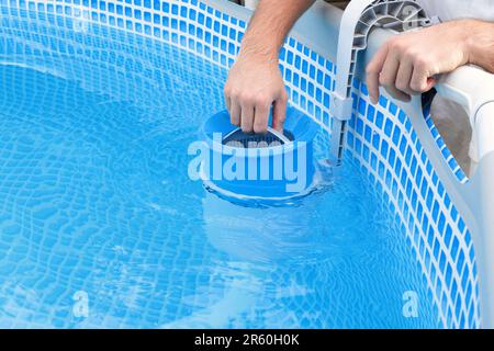 L'uomo pulisce lo skimmer per la piscina di telaio. Pulizia piscina contaminata. Foto Stock