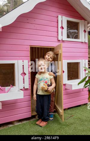 Bambini, ragazzi e ragazze, giocando in casa di legno rosa per i bambini nel cortile Foto Stock