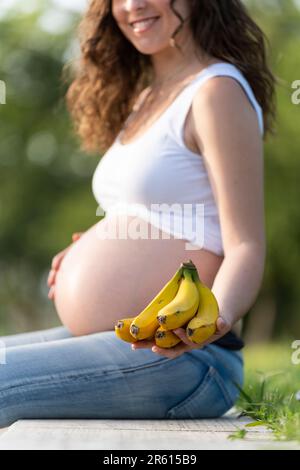 Donna incinta che tiene alcune banane e che mostra alla fotocamera Foto Stock