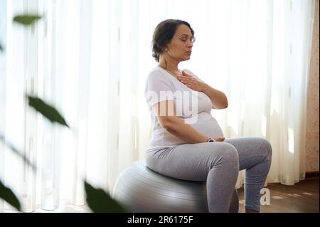 Gravidanza facendo esercizi di respirazione per una gravidanza sana, prepara il corpo per il parto, mettendo le mani del petto e della pancia Foto Stock