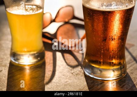 Primo piano di due bicchieri di birra fresca con occhiali da sole sullo sfondo di un tavolo di legno Foto Stock