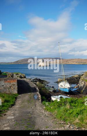 Scozia, Ebridi esterne, Isola di barra, Baia del Castello, Castello di Kisimul visto dalla riva con barche ormeggiate in primo piano. Foto Stock