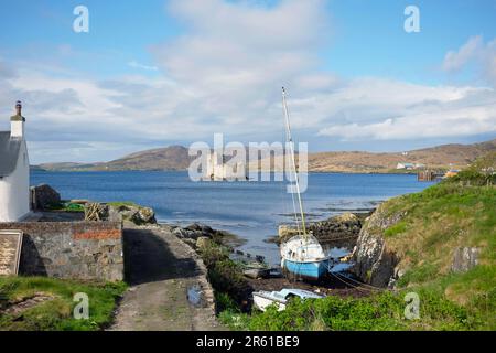 Scozia, Ebridi esterne, Isola di barra, Baia del Castello, Castello di Kisimul visto dalla riva con barche ormeggiate in primo piano. Foto Stock