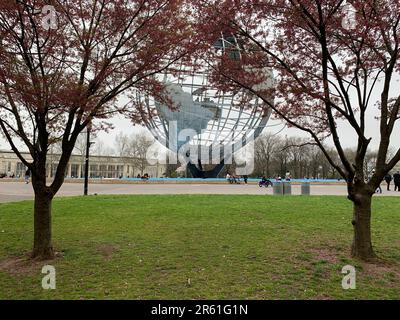 Le persone si riuniscono intorno all'Unisfero, un punto di riferimento della Fiera dei Mondi di New York del 1964, circondato da alberi di ciliegio in fiore nel Queens New York City Foto Stock