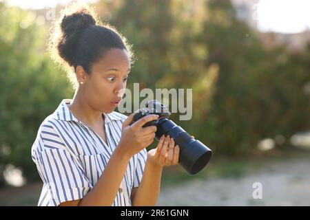 Sorpreso nero fotograper controllo risultato su mirrorless fotocamera in un parco Foto Stock