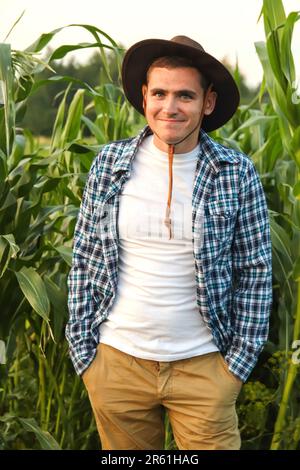 Contadino divertente in posa nel campo di mais. Caucasico calmo coltivatore di mais maschio in passeggiate lungo il campo di mais. Giovane cowboy sorridente. Verticale. Giovane divertente Foto Stock