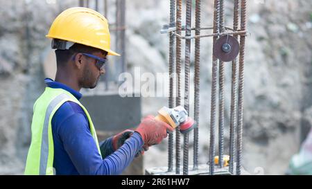 Nei concetti di costruzione, un lavoratore di costruzione che lavora in cantiere in un elmetto giallo punta a una smerigliatrice angolare in mano. Professionale Foto Stock