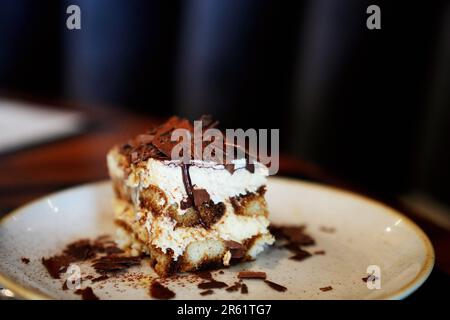 Un piatto bianco con un tradizionale dessert italiano di tiramisù, delicatamente condito con scaglie di cioccolato per una maggiore consistenza e sapore Foto Stock