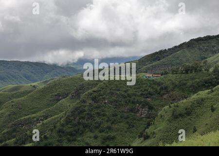 Uno splendido paesaggio con una casa in una lussureggiante catena montuosa verde, alberi alti e lussureggiante erba verde Foto Stock