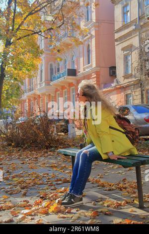 La foto è stata scattata nella città di Odessa. Nella foto, una giovane donna turistica con uno zaino riposa su una panchina in un parco autunnale. Foto Stock