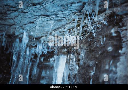 Un primo piano di una parete rocciosa con diversi ghiaccioli appesi Foto Stock