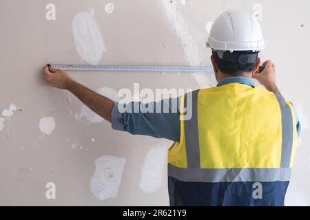 Architetto professionista in gilet giallo mette nastro-linea a muro di scaby per misurare la distanza Foto Stock