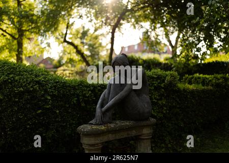 Una scultura in pietra raffigurante una figura femminile seduta, le braccia incrociate sulle gambe Foto Stock