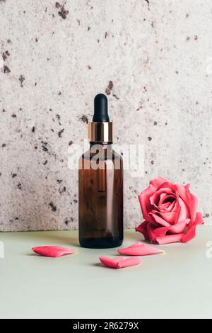 Bottiglia di siero marrone e fiore di rosa su fondo di pietra naturale. Primo piano. Foto Stock