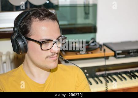 Giovane uomo con gli occhiali che si divertiva mentre ascoltava il suo disco in vinile con gli auricolari vintage nella sua stanza Foto Stock