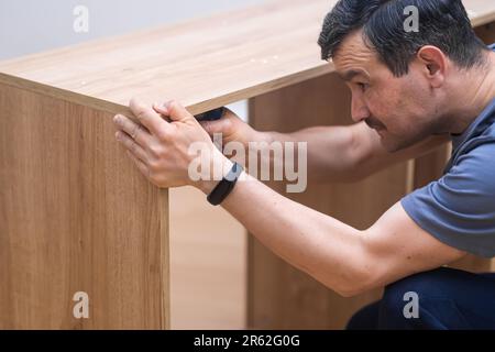 I servizi di assemblaggio di mobili hanno messo a fuoco l'uomo nel montaggio uniforme professionale parti di scaffale Foto Stock
