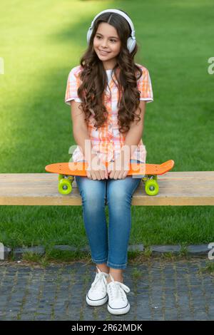 ragazza felice con skateboard all'aperto. ragazza teen con skateboard in cuffie Foto Stock