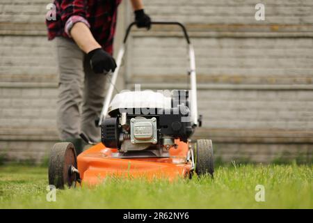 L'uomo irriconoscibile del giardiniere nei guanti di protezione avvia il rasaerba prima di tagliare il prato verde nel suo cortile. Uomo con rasaerba motorizzato ca Foto Stock