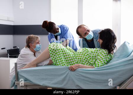 Donna incinta urla forte durante la nascita del bambino, in piedi con marito accanto a lei per il conforto durante la chirurgia cesareo in reparto ospedaliero. Futura madre con contrazioni dolorose Foto Stock