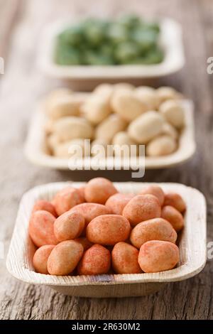 Arachidi rosse rivestite in stile giapponese croccanti o cracker con sapore di peperoncino in un piccolo recipiente monouso con foglie di palma (profondità di campo molto bassa) Foto Stock