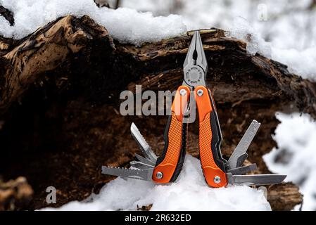 Pinza multifunzione con altri attrezzi e coltello su un vecchio albero cavo ricoperto di neve. Messa a fuoco selettiva. Foto Stock