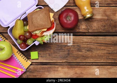 Composizione piatta con pranzo al sacco, gustoso cibo sano e cancelleria scolastica su tavolo di legno. Spazio per il testo Foto Stock