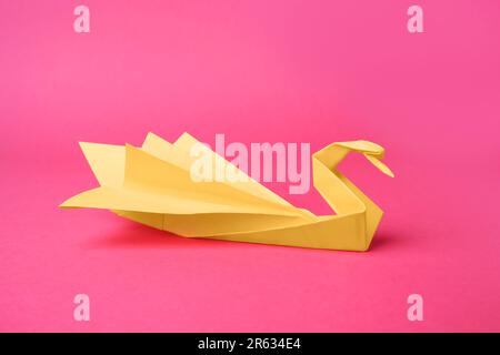 Cigno di carta giallo su sfondo rosa. Origami arte Foto Stock