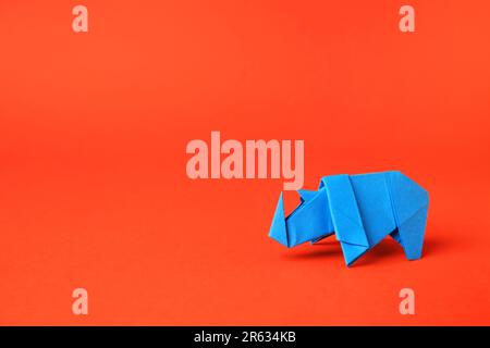 Origami art. Rinoceronti di carta blu chiaro fatti a mano su sfondo arancione, spazio per il testo Foto Stock