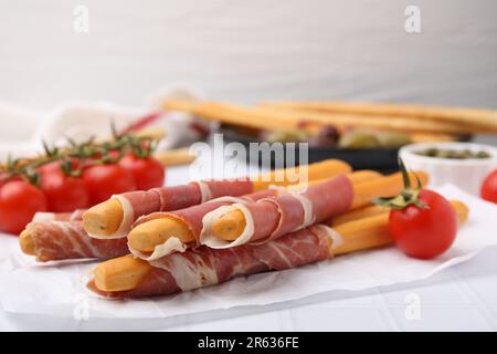 Deliziosi bastoncini di grissini con prosciutto e spuntini su tavola bianca, primo piano Foto Stock