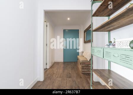 Bella sala d'ingresso di una casa con una porta di fronte blu, pavimenti in legno, mobili in stile industriale e uno specchio con una grande cornice dorata Foto Stock