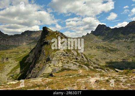 Uno stretto sentiero che sale sul ripido pendio di un'alta montagna che domina pittoresche scogliere in una nuvolosa giornata estiva. Parco naturale Ergaki, Krasnoya Foto Stock