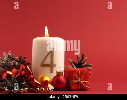 Quarta candela di Avvento brucia, candela bianca con il numero quattro su uno sfondo rosso, decorazione di Natale, spazio per il testo Foto Stock